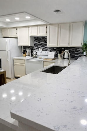 Una cocina moderna con armarios blancos, salpicadero blanco y negro, encimera de mármol y electrodomésticos de acero inoxidable.
