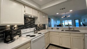 A modern kitchen with white cabinets, a black and gray backsplash, a stove, and a coffee maker. - Beach View Condo 106 By The Beach  Heated Pool Hot tub (South Padre Island)