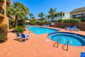 A swimming pool with lounge chairs, palm trees, and a brick patio.