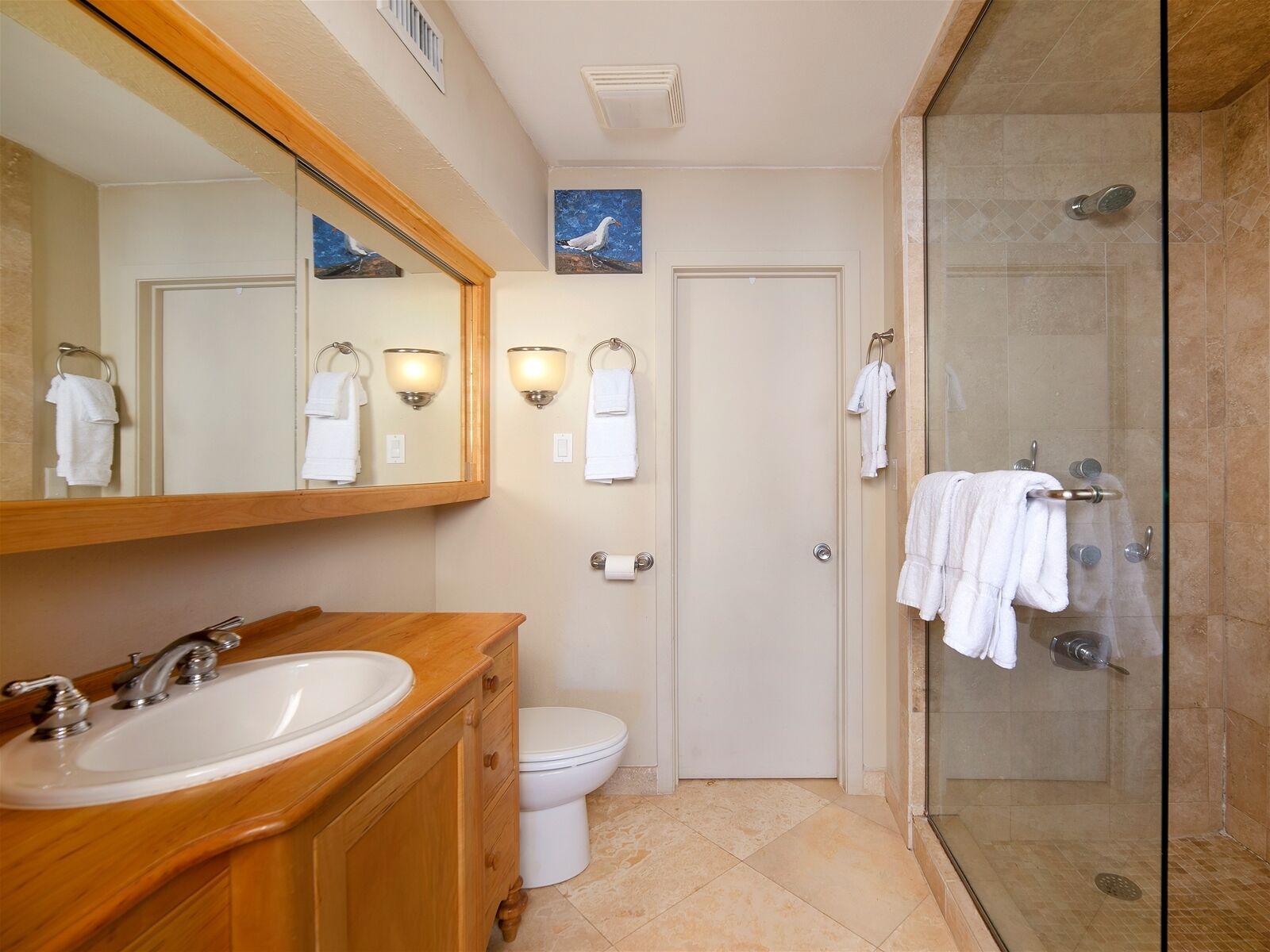 Une salle de bain avec un meuble-lavabo en bois, un lavabo blanc, des toilettes, une cabine de douche en verre et une porte dotée d’un porte-serviettes.