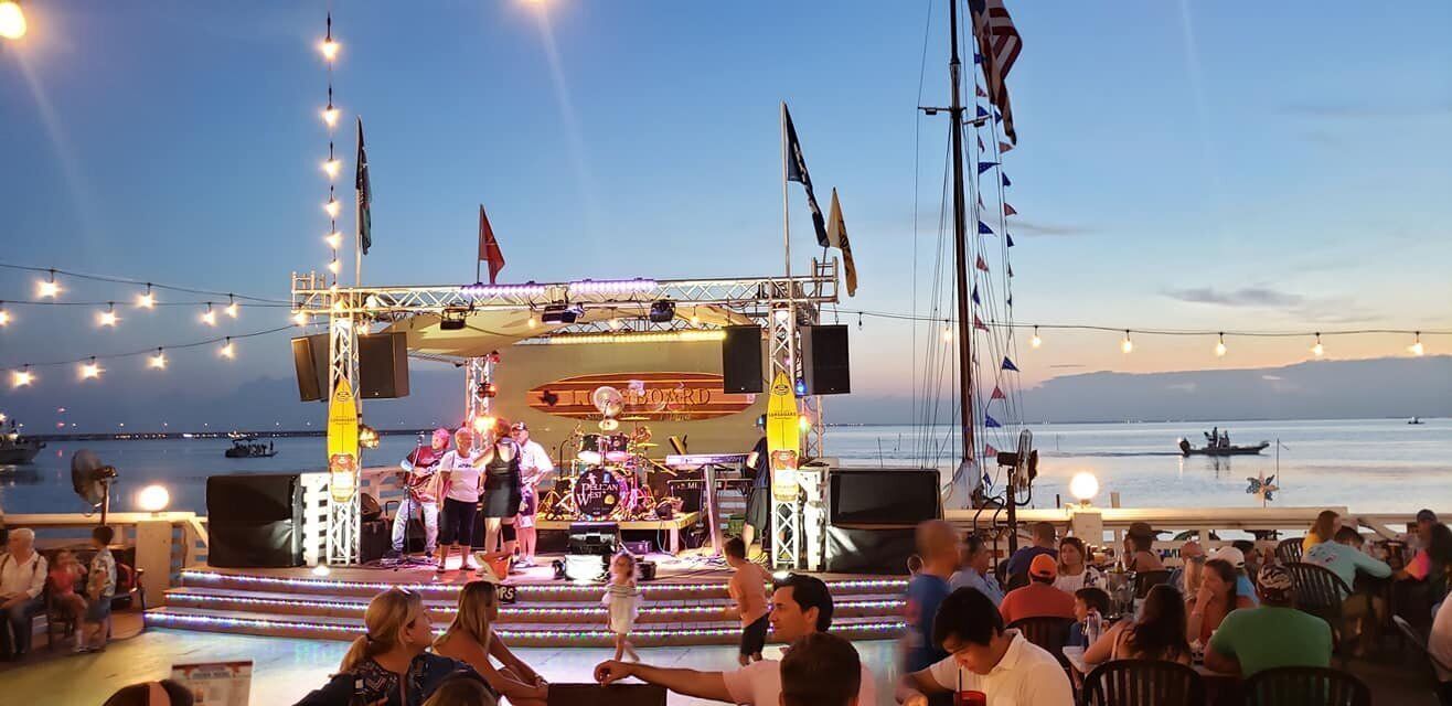 A stage with musicians performing at a beachside event, surrounded by an audience.