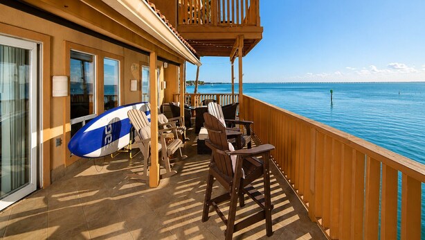 A balcony with a view of the sea, wooden furniture, and a surfboard. - La Solana 118 A Bayview paradise - approved pets only (South Padre Island)