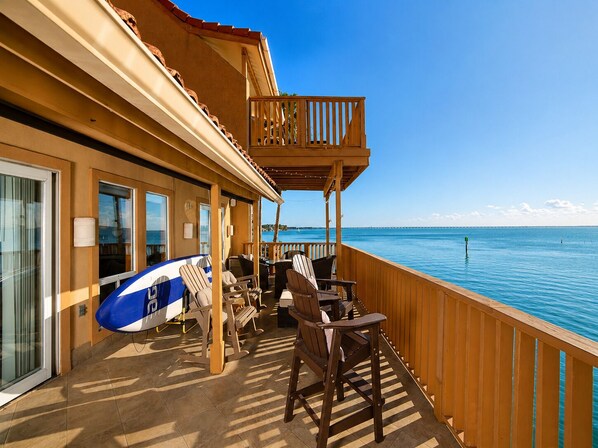 A balcony with a view of the sea, wooden furniture, and a surfboard.