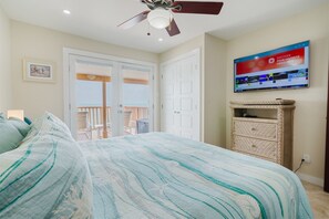 Quarto com cama, ventilador de teto, TV fixada na parede e varanda com cadeiras.