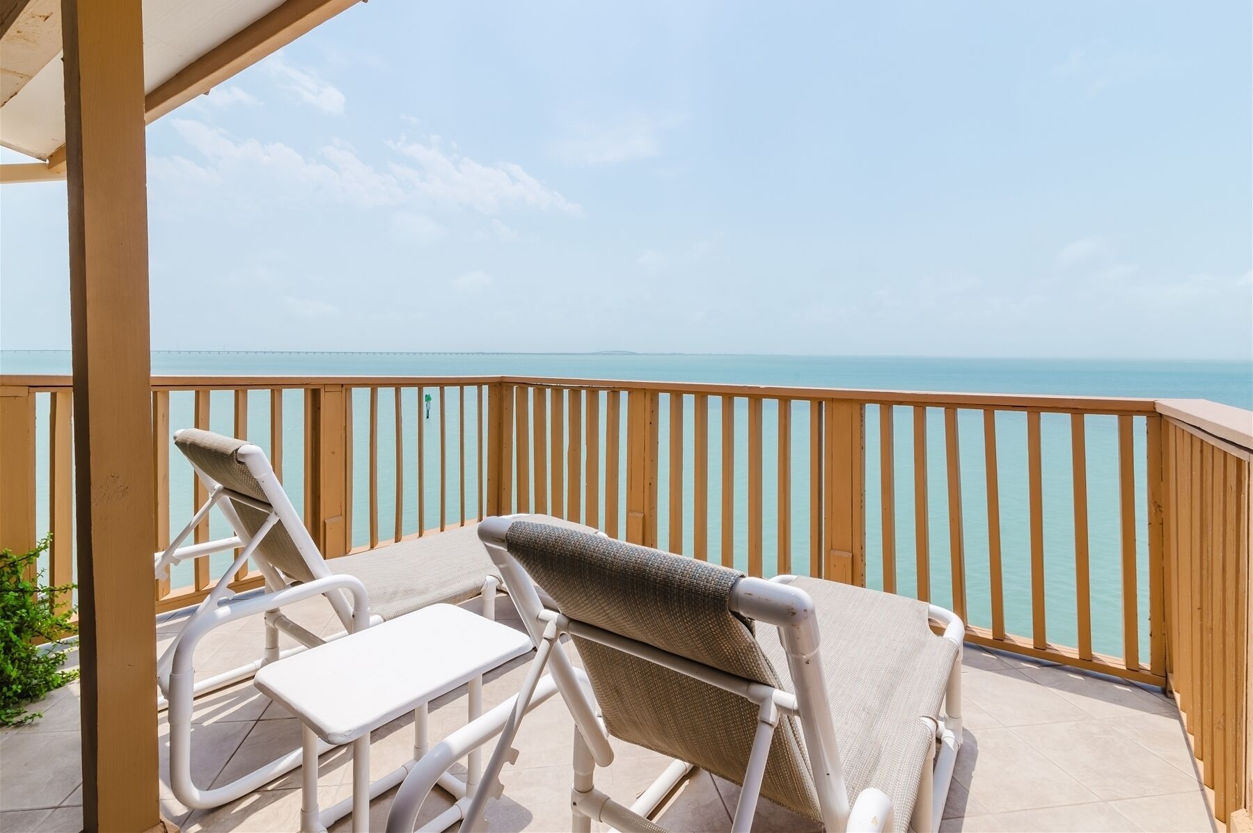 A balcony with two lounge chairs and a small table, overlooking a calm sea and clear sky.