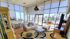 A spacious living area with a large window, a sofa, a coffee table, and a television. - Sunchase Resort Condo 20 ft glass view 4-min to water (South Padre Island)