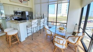 A modern kitchen with a central island, bar stools, and a dining table with chairs. - Sunchase Resort Condo 20 ft glass view 4-min to water (South Padre Island)