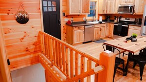 A wooden interior with a kitchen, dining area, and a staircase. - Treetop Escape | Hot Tub, Hiking, Movie Theater & 5 Private Acres! (Logan)