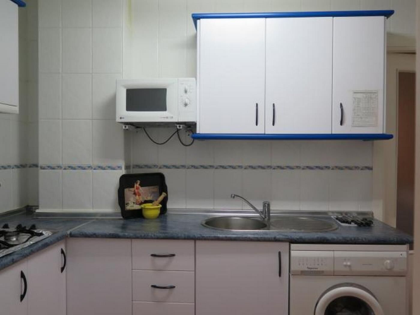 Une cuisine avec des meubles blancs, un four à micro-ondes, un évier et un lave-linge.