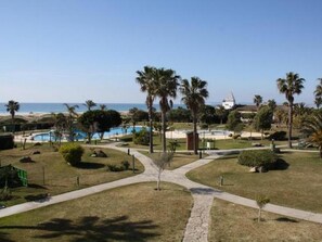 Relax by the pool surrounded by lush gardens and palm trees, with the ocean visible in the distance.