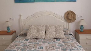 Ein Schlafzimmer mit einem Bett, zwei Nachttischen, einem Kopfteil, einem an der Wand befestigten Hut und einem Bild einer Strandansicht.