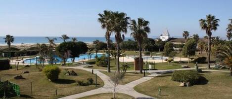 A resort with a pool, palm trees, and a view of the ocean.