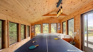 Una sala in legno con ampie finestre e un lampadario, dove è presente un tavolo da ping pong.
