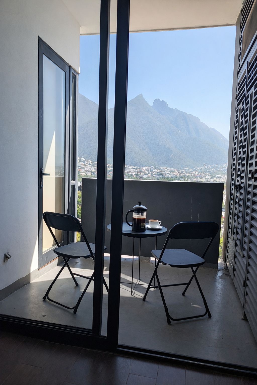 A balcony with two chairs and a table, a coffee pot, and a view of a mountain.