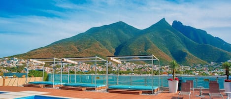 A swimming pool with sun loungers and a mountain backdrop.