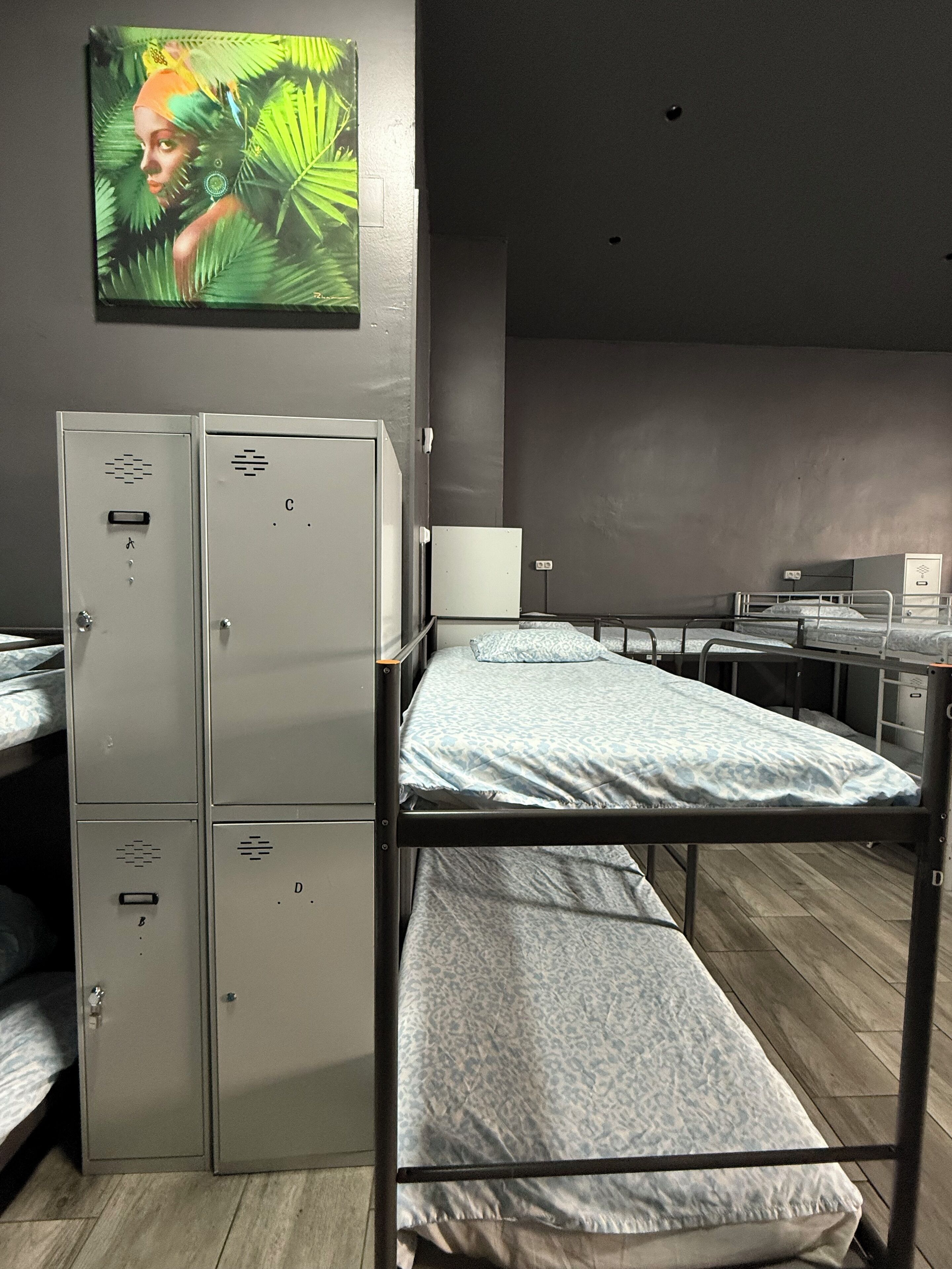 A dormitory room with bunk beds, a small desk, a whiteboard, and metal lockers.