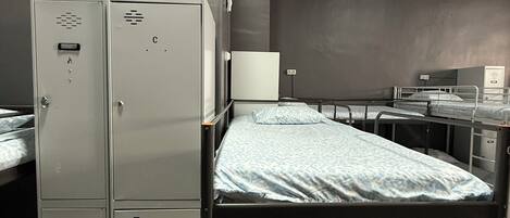A dormitory room with bunk beds, a small desk, a whiteboard, and metal lockers.