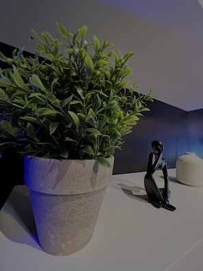 A potted plant in a large, textured pot, a minimalist sculpture, and a white, modern seating area.