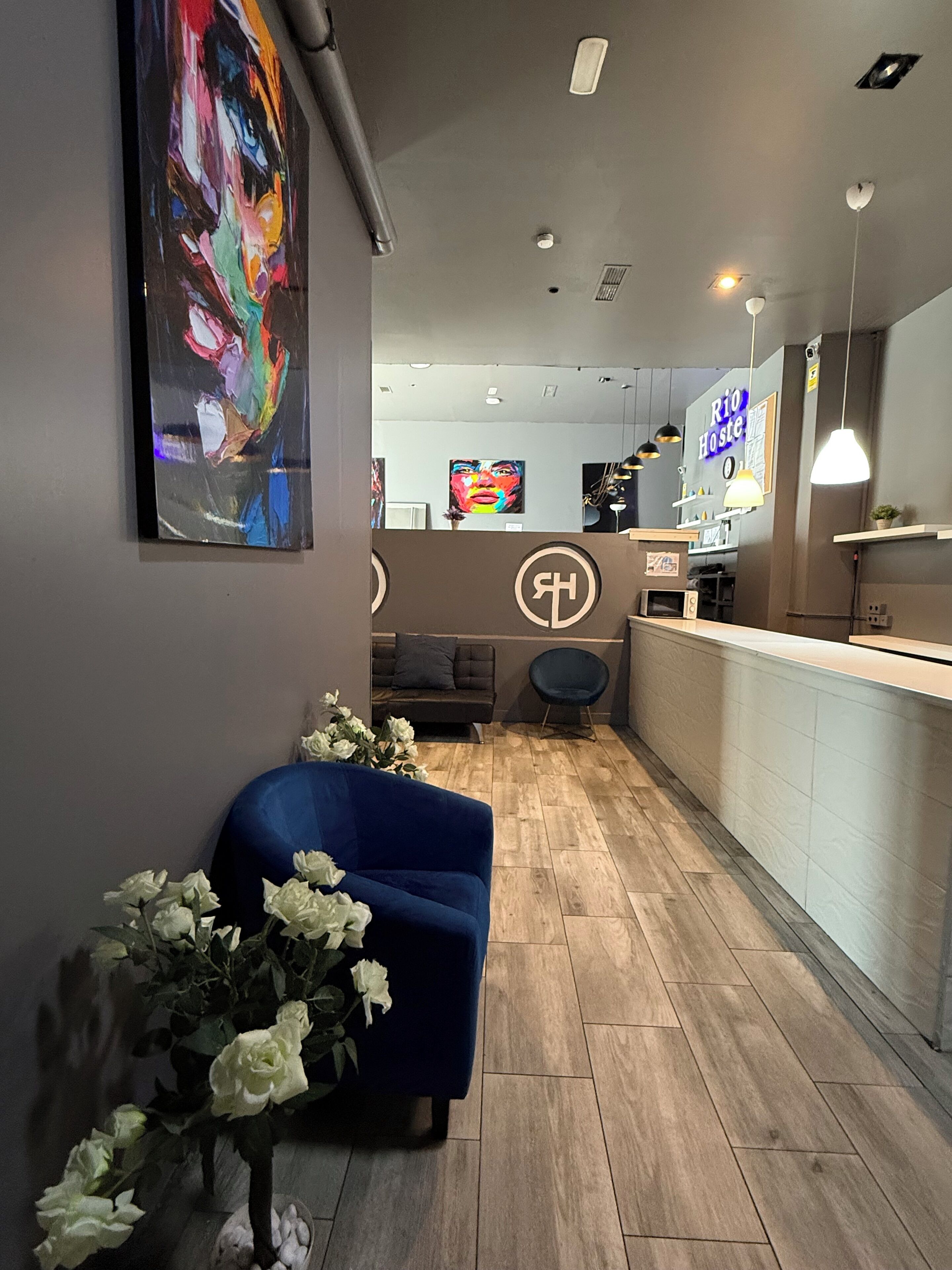 A modern interior with a reception desk, a blue armchair, a floral arrangement, and a colorful abstract painting on the wall.