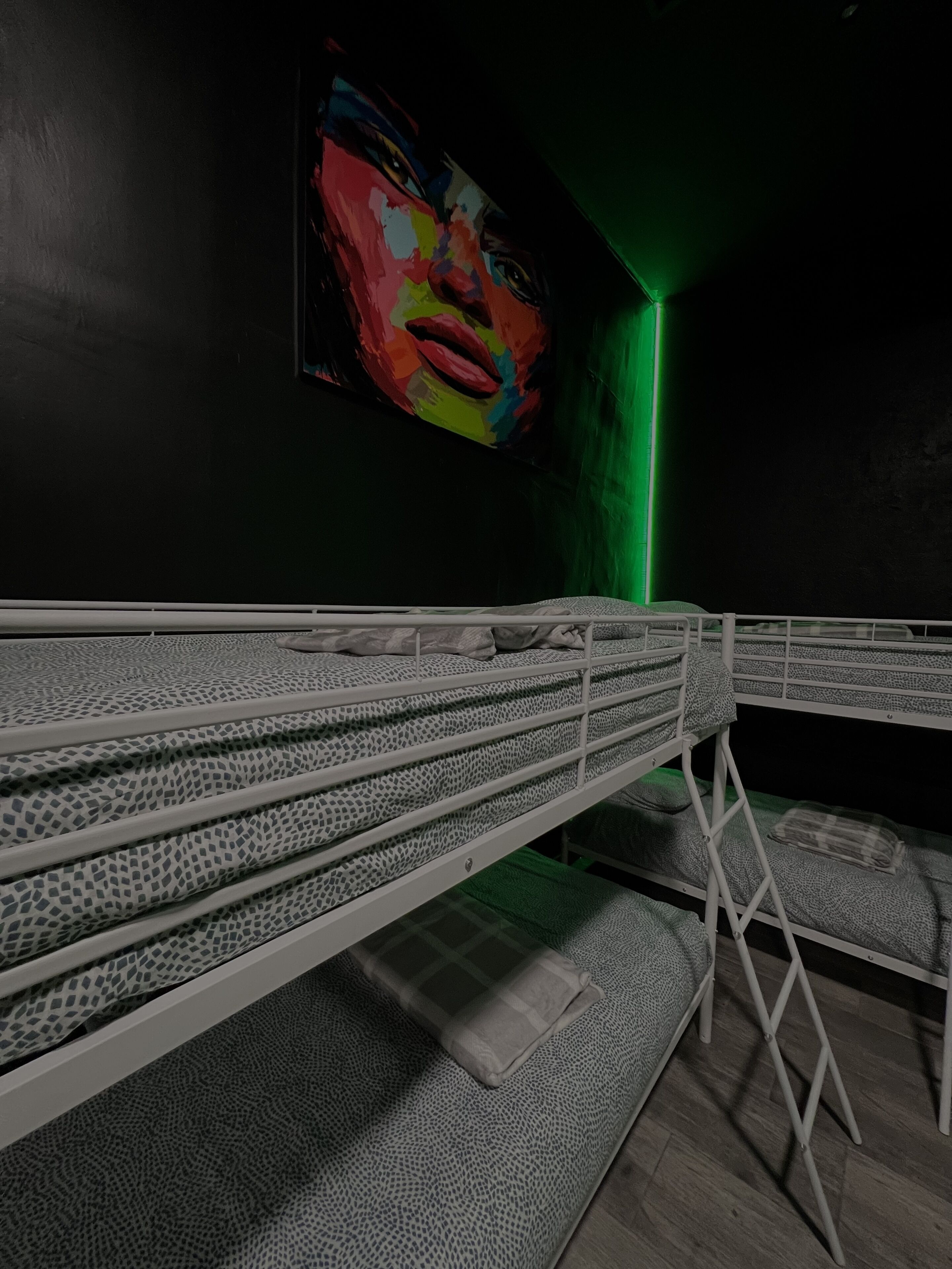 Una habitación con literas, una luz verde y un cuadro abstracto y colorido en la pared.