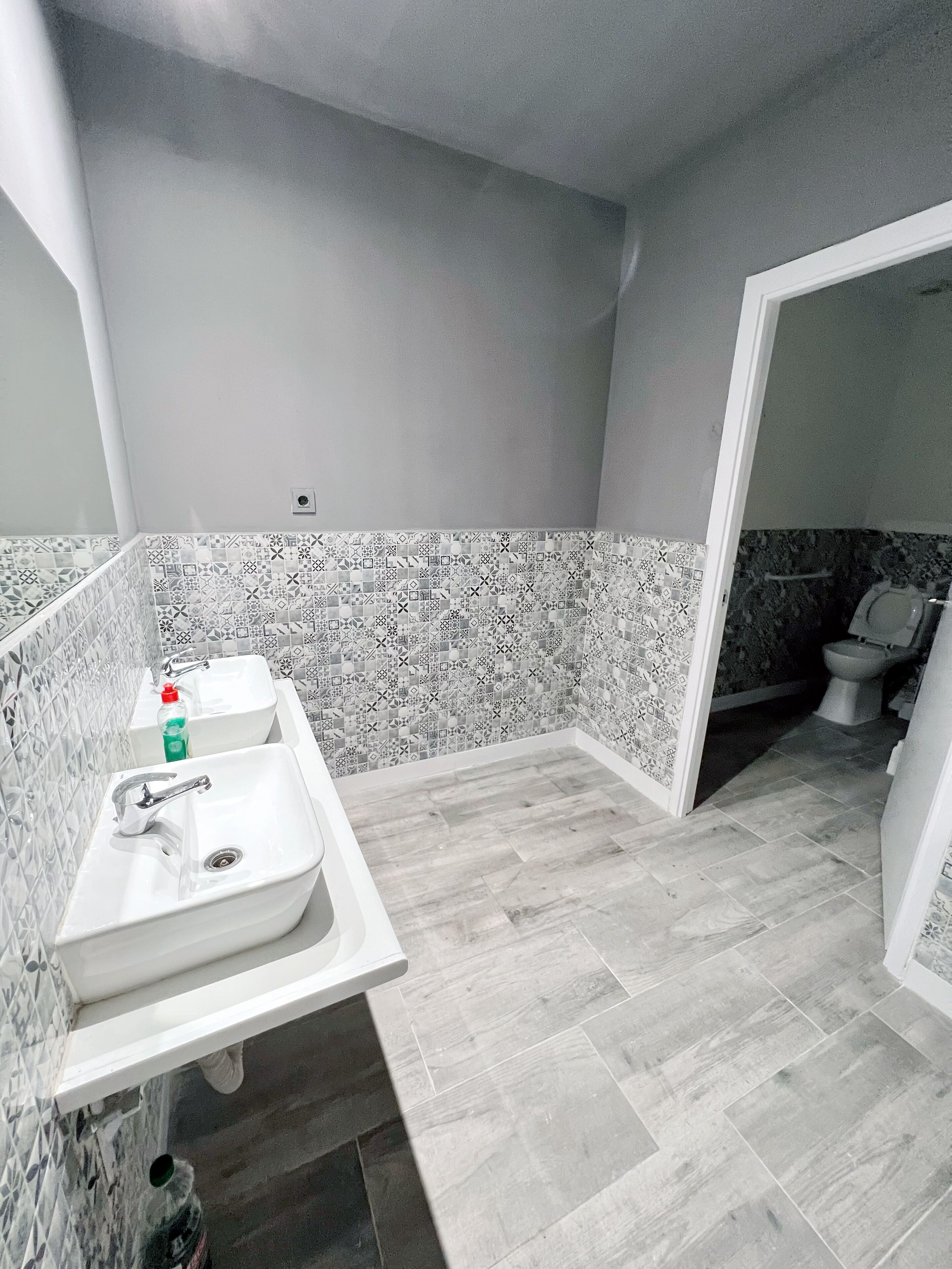 Un baño con lavamanos blanco, un espejo y un inodoro. Las paredes están cubiertas de azulejos con un diseño geométrico.