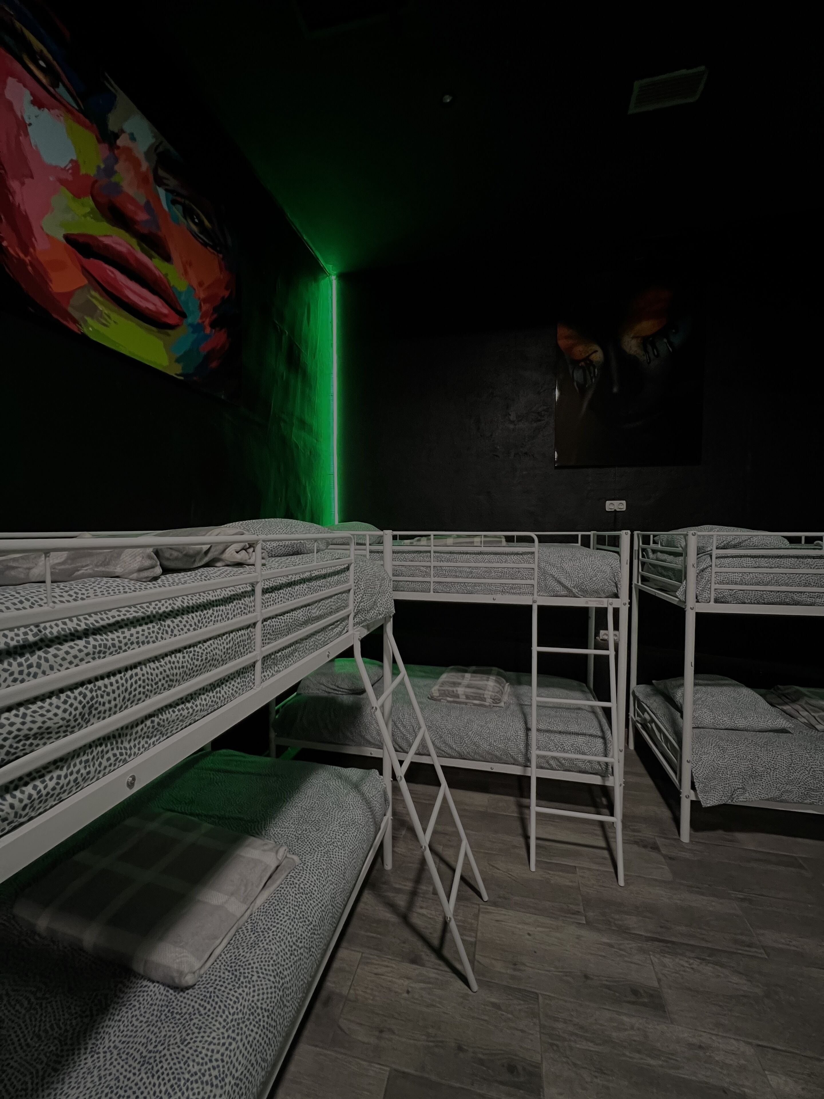 Una habitación con literas, una luz verde y un cuadro de colores en la pared.
