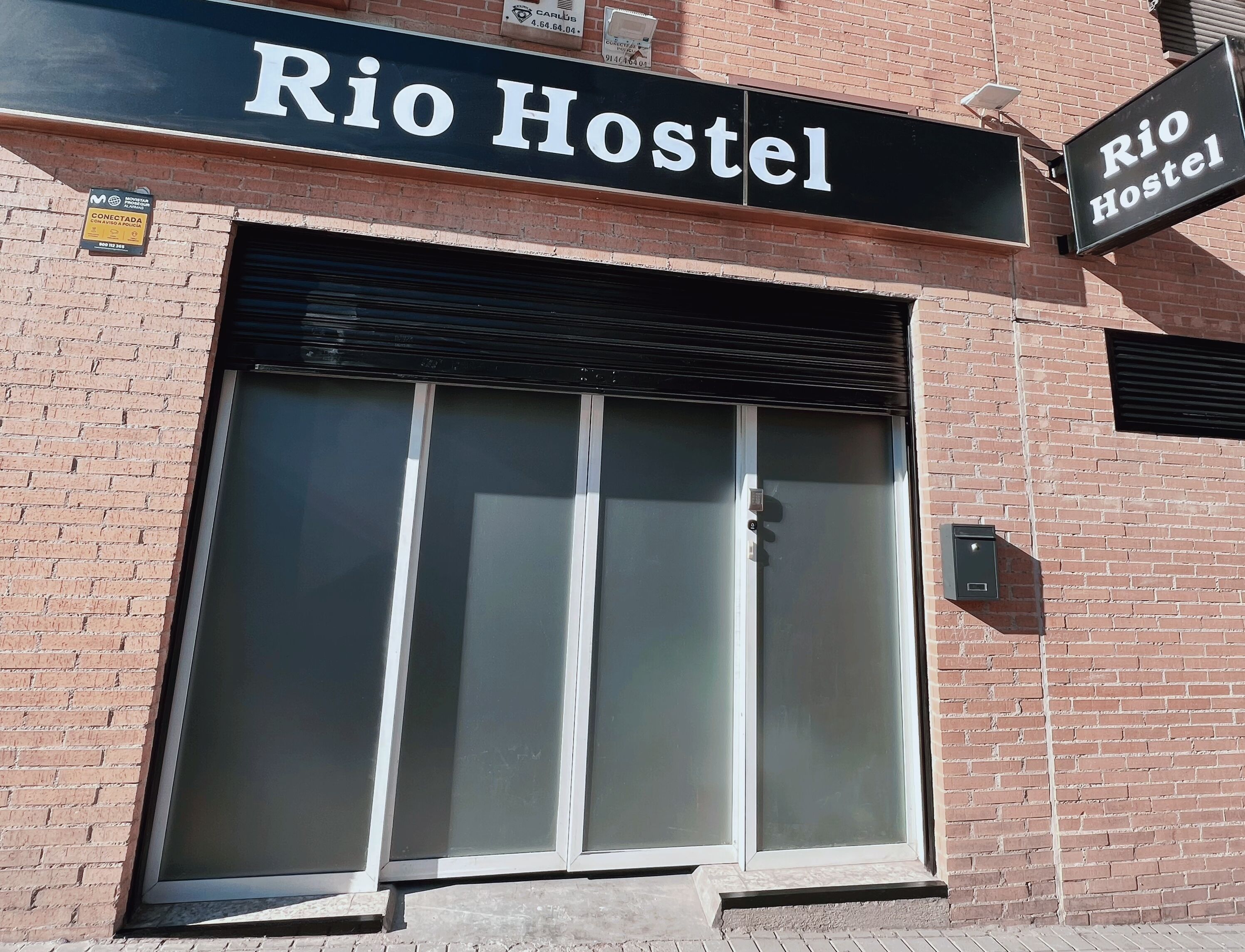 A brick building with a large glass door and a sign that reads "Rio Hostel".