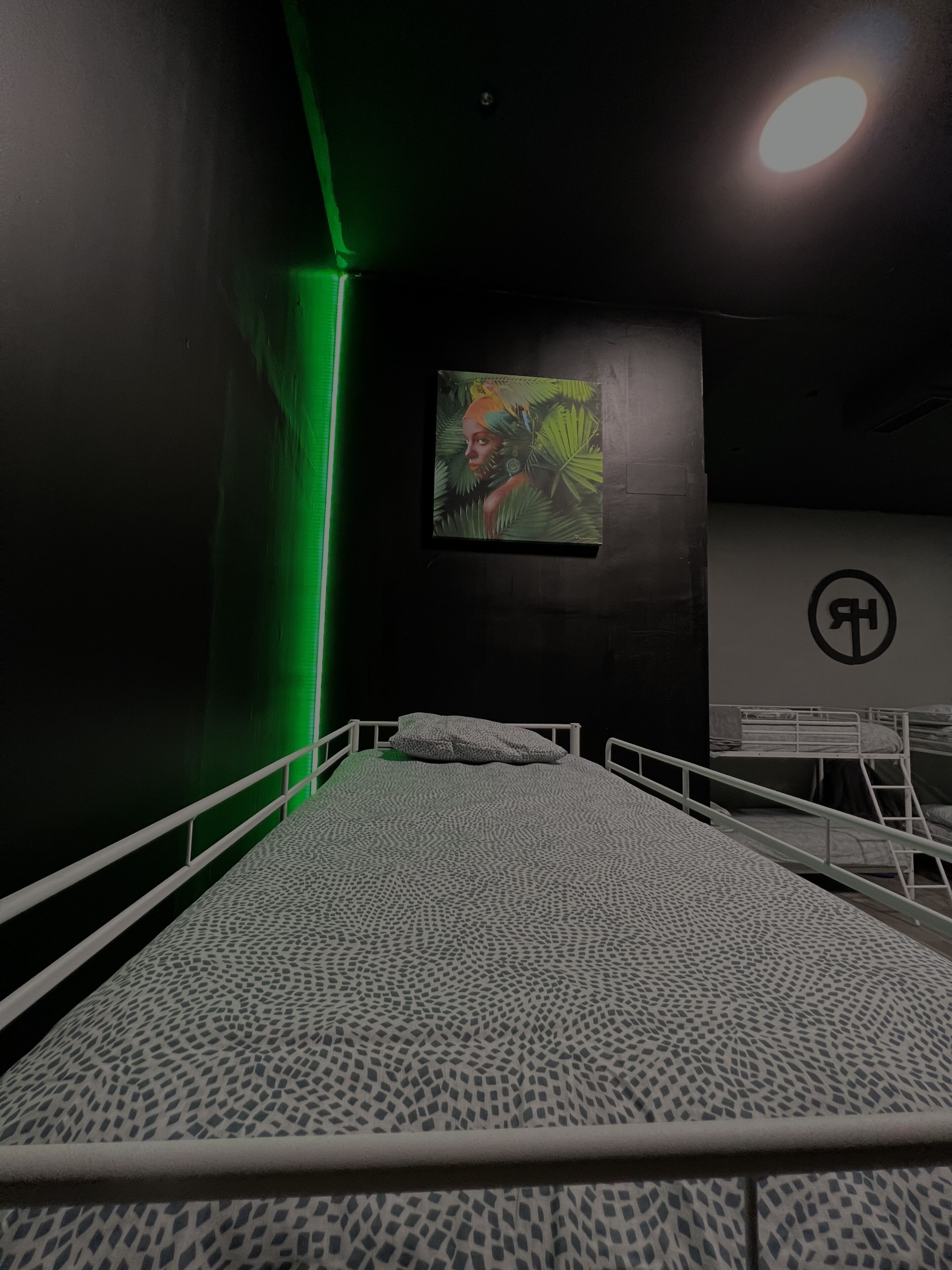 A single bed with a patterned bedspread, a green wall, and a painting of a woman in a jungle setting.