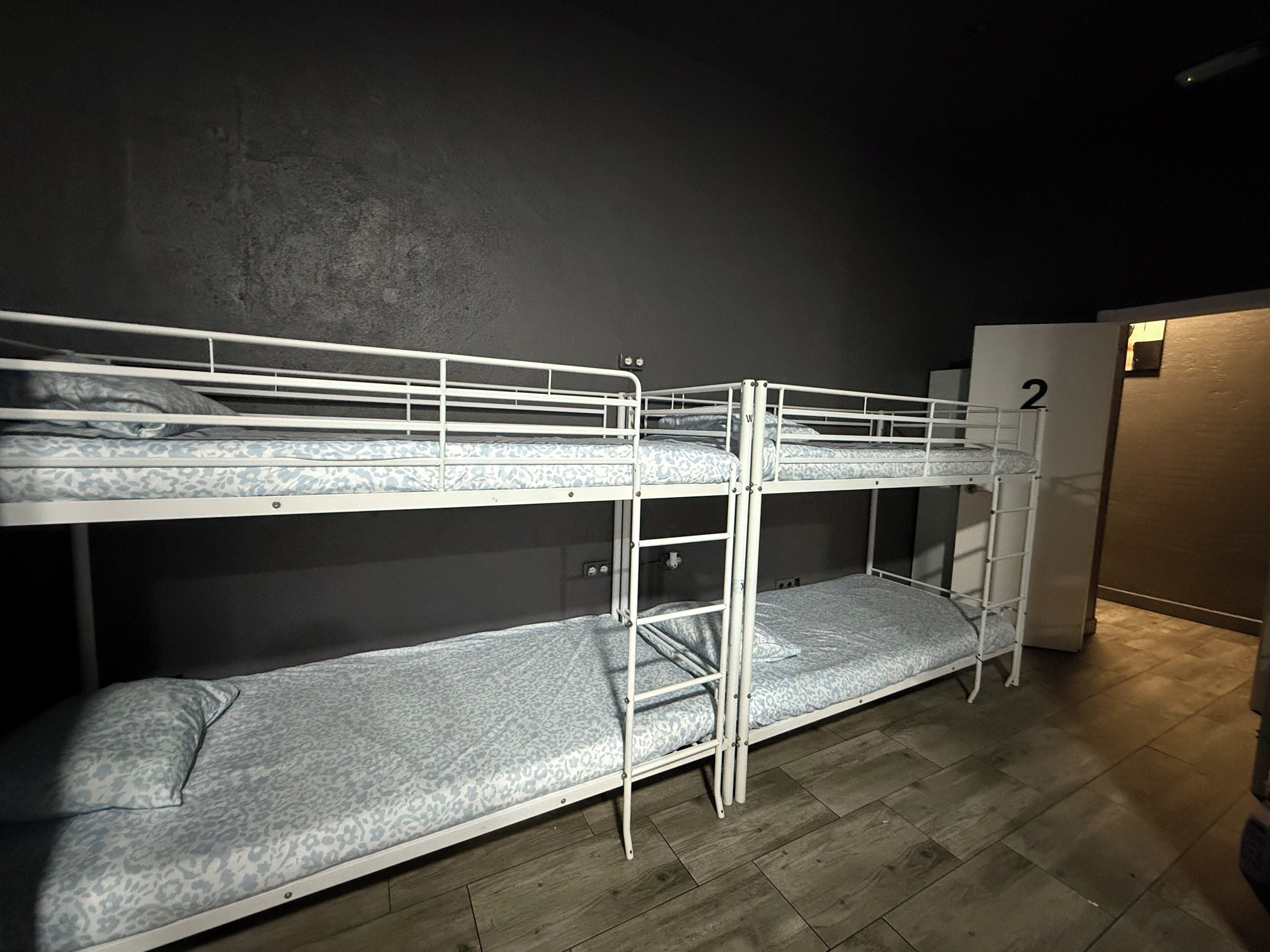 Bunk beds with a mattress and pillows, a wooden floor, and a door with the number 2.