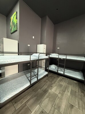 A dormitory room with bunk beds, a small white cabinet, and a wall-mounted power outlet.
