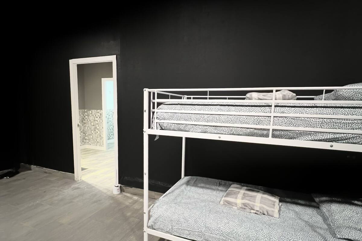A bunk bed with patterned bedding in a room with wooden flooring and a dark wall.