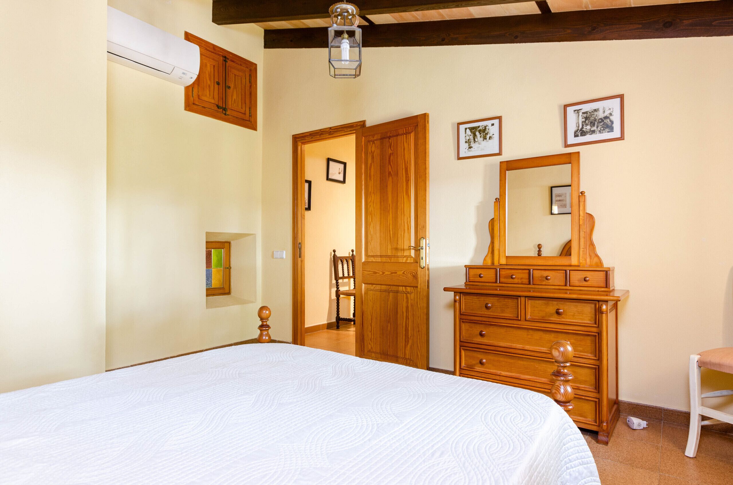 Een slaapkamer met een bed, een houten dressoir en een spiegel.