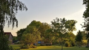A grassy field with trees and a stone building in the background. - Cottage Le Merle Blanc 2 to 6 persons (PIERREPONT)