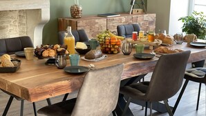Un comedor con una mesa de madera lista para el desayuno, que incluye pan, bollería, frutas y bebidas.