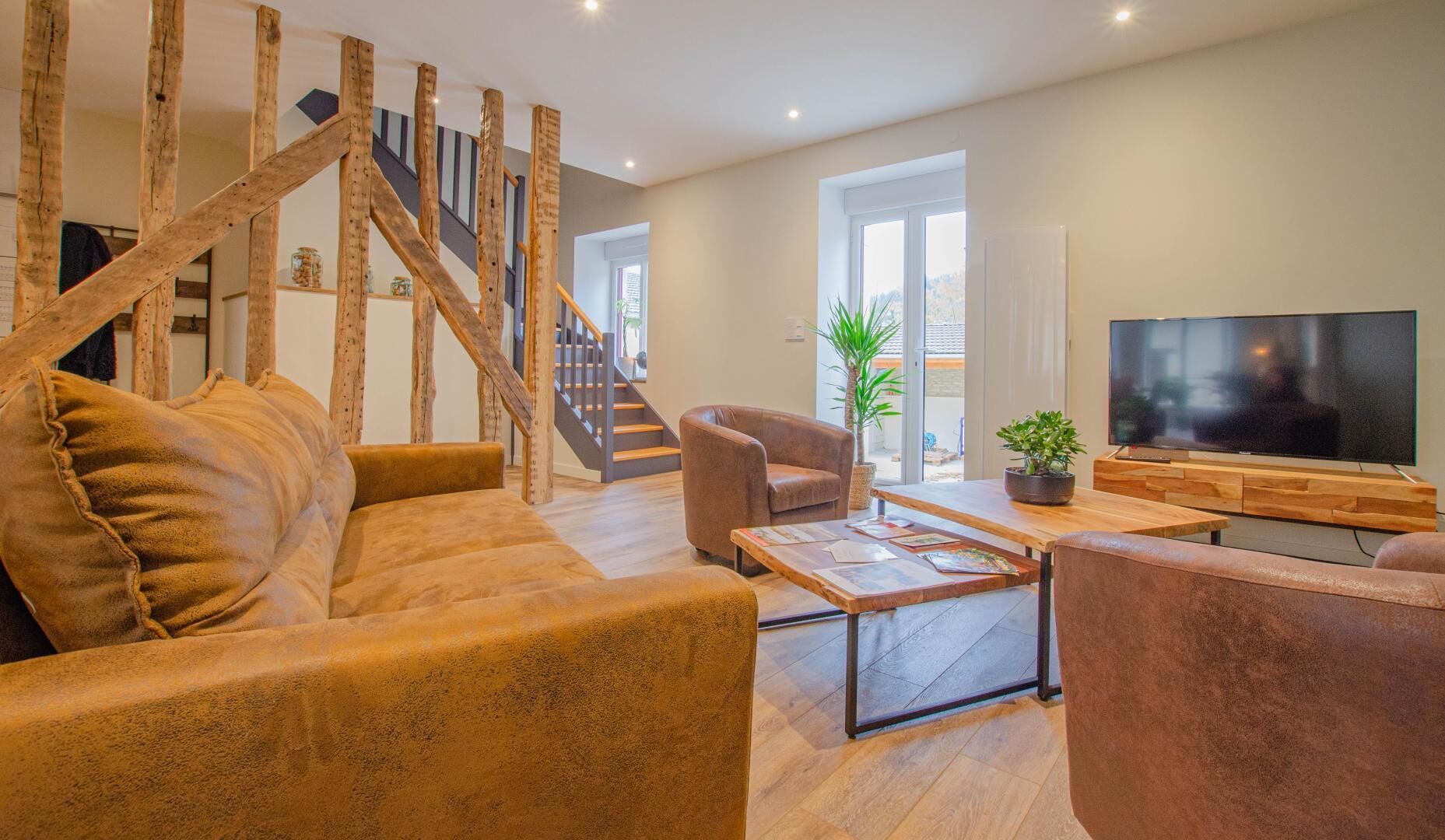 Ein modernes Wohnzimmer mit einer Holztreppe, einem Sofa, einem Couchtisch, einem Fernseher und einer Topfpflanze.