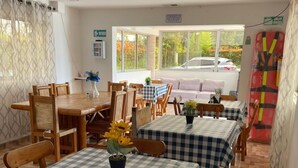 Un espace repas avec des nappes à carreaux, des chaises en bois et une vue sur l’extérieur.