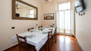 Comedor con mesa dispuesta para seis comensales, una araña, televisor en la pared y puerta que da al exterior.