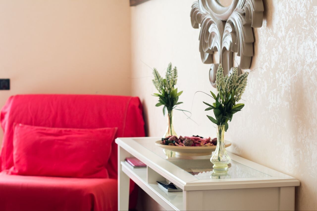 Una sala de estar con un sofá rojo, una mesita auxiliar blanca con un bol de aperitivos, y dos jarrones con plantas.