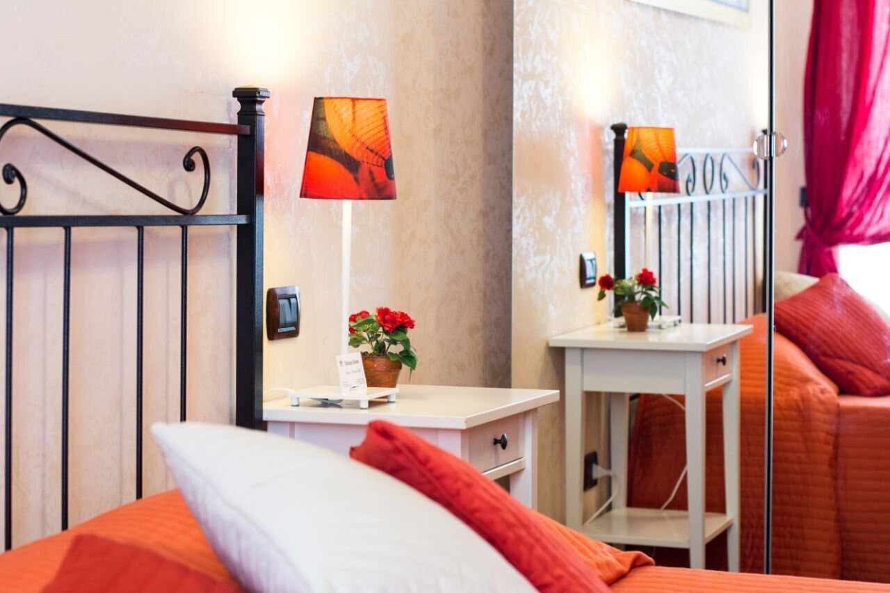 Ein Hotelzimmer mit einem Bett, einem Nachttisch mit Lampe, einem kleinen Tisch mit Blumentopf und einem Spiegel.