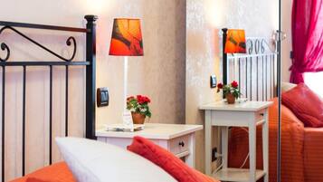 Ein Hotelzimmer mit einem Bett, einem Nachttisch mit Lampe, einem kleinen Tisch mit Blumentopf und einem Spiegel.