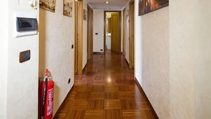 Un pasillo con suelo de madera, un extintor y un cuadro en la pared.