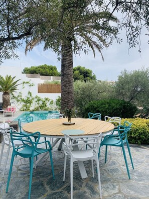 An outdoor dining area with a round wooden table surrounded by white and turquoise chairs. - Villa like an oasis with Mediterranean garden and heated pool in Cadaqués (Cadaqués)