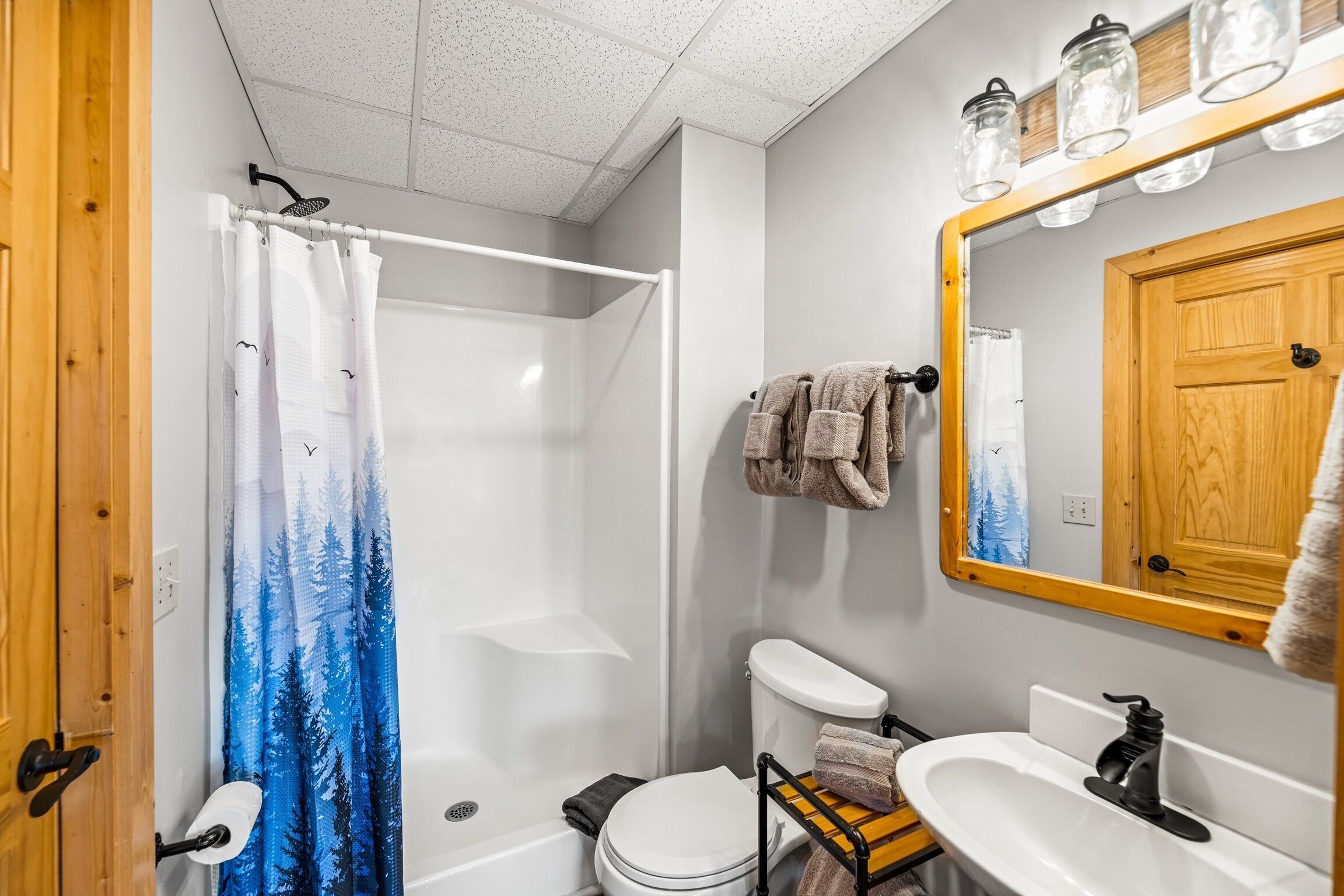 Ein Badezimmer mit Dusche, Toilette, Waschbecken und einem Spiegel mit Holzrahmen.