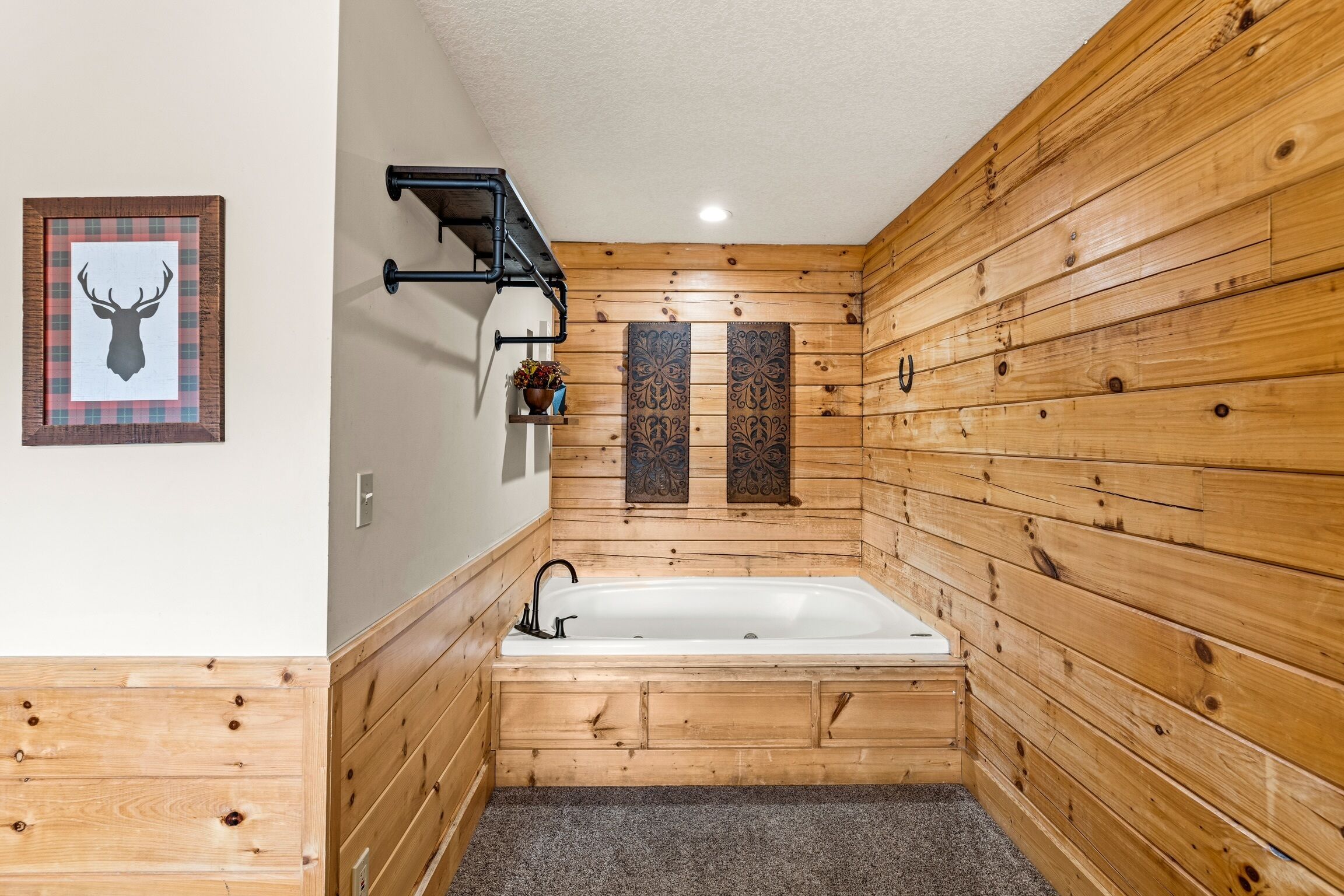 A wooden-paneled bathroom with a bathtub, a framed deer head artwork, and decorative wall panels.