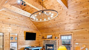A cozy wooden cabin interior with a pool table, a fireplace, and a television mounted on the wall.