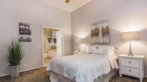 A bedroom with a large bed, two bedside tables with lamps, a door leading to another room, and a wall-mounted painting. - Quiet and cozy condo near Laguna (Aliso Viejo)