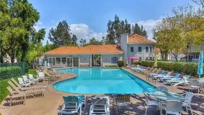 A swimming pool with lounge chairs and umbrellas, surrounded by a building with a tiled roof. - Quiet and cozy condo near Laguna (Aliso Viejo)