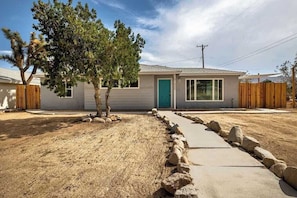 A single-story house with a front door, windows, and a small tree in the yard. - Audrey's Place, New Hot Tub, Mins to Joshua Tree (Joshua Tree)