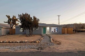 A single-story house with a front yard, a small tree, and a gravel driveway. - Audrey's Place, New Hot Tub, Mins to Joshua Tree (Joshua Tree)