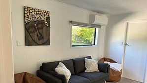 Un salon moderne avec un canapé gris foncé, deux coussins blancs à motifs, un pouf marron et un tapis coloré.